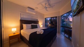 Ein Hotelzimmer mit Bett, Nachttischlampen, Deckenventilator und Blick ins Freie.