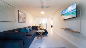 Ein modernes Wohnzimmer mit einer Couch, einem an der Wand befestigten Fernseher und einem Deckenventilator.