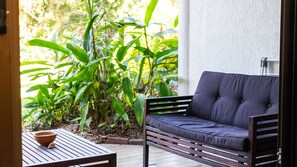 Eine Terrasse mit einem dunkelgrauen Sofa und einem Holztisch, auf dem sich eine Schale befindet, sowie ein Garten mit verschiedenen Pflanzen.