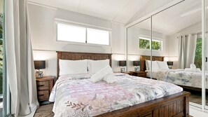 A bedroom with a large bed, two bedside tables, a nightstand, a mirror, and a window with curtains. - Tropical Retreat on Reid (Wongaling Beach)
