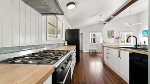 A kitchen with a wood countertop, a stove, and white cabinetry. - Tropical Retreat on Reid (Wongaling Beach)