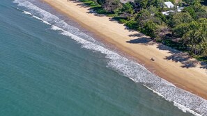 An aerial view of a beach with a clear demarcation between the water and the sand, a few trees, and a small structure on the sand. - Tropical Retreat on Reid (Wongaling Beach)