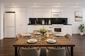 Une cuisine moderne avec des meubles blancs, un plan de travail noir et une table à manger pour six personnes.