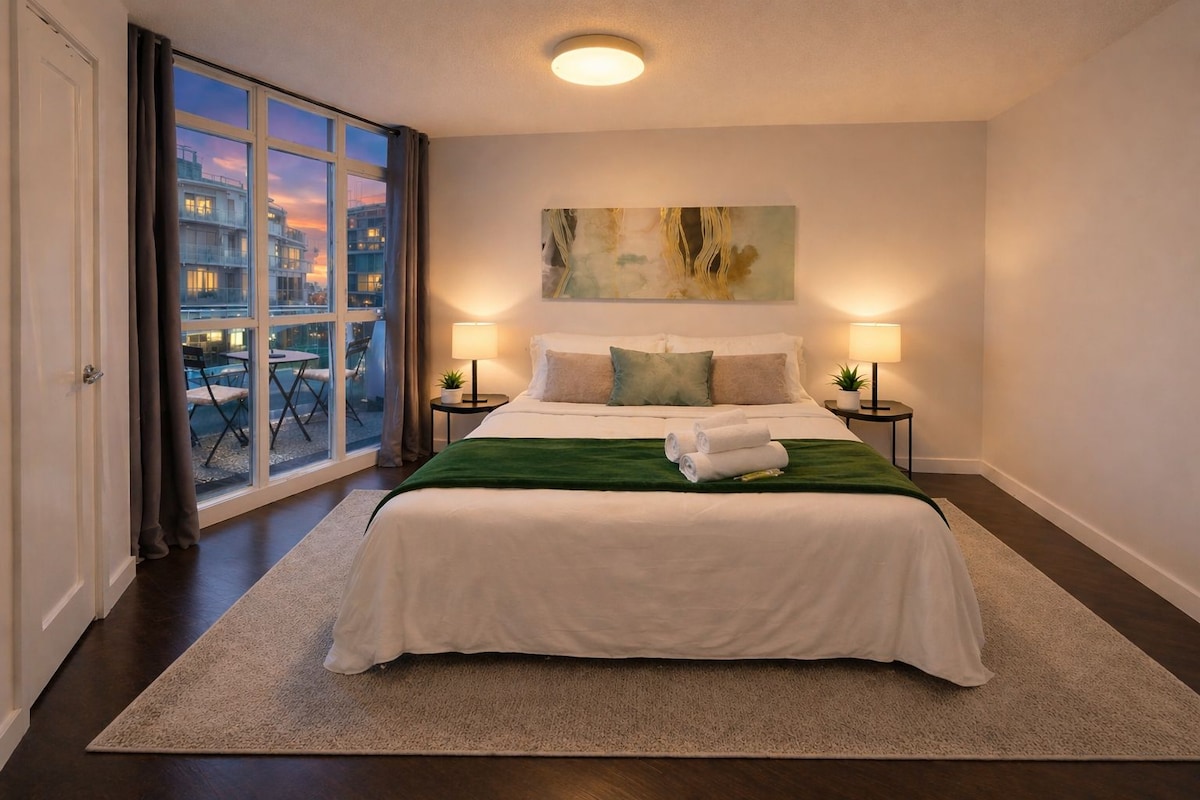 Une chambre d’hôtel avec un grand lit, deux tables de chevet avec des lampes, un plaid vert et un tableau au mur.