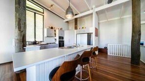 A modern kitchen with a large island, wooden chairs, and a hanging light fixture. - Island Vista Retreat (South Mission Beach)