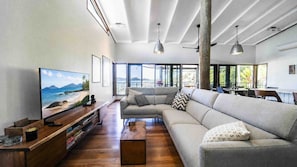 A spacious living area with a large sofa, a wooden coffee table, and a flat-screen TV displaying a scenic beach view. - Island Vista Retreat (South Mission Beach)