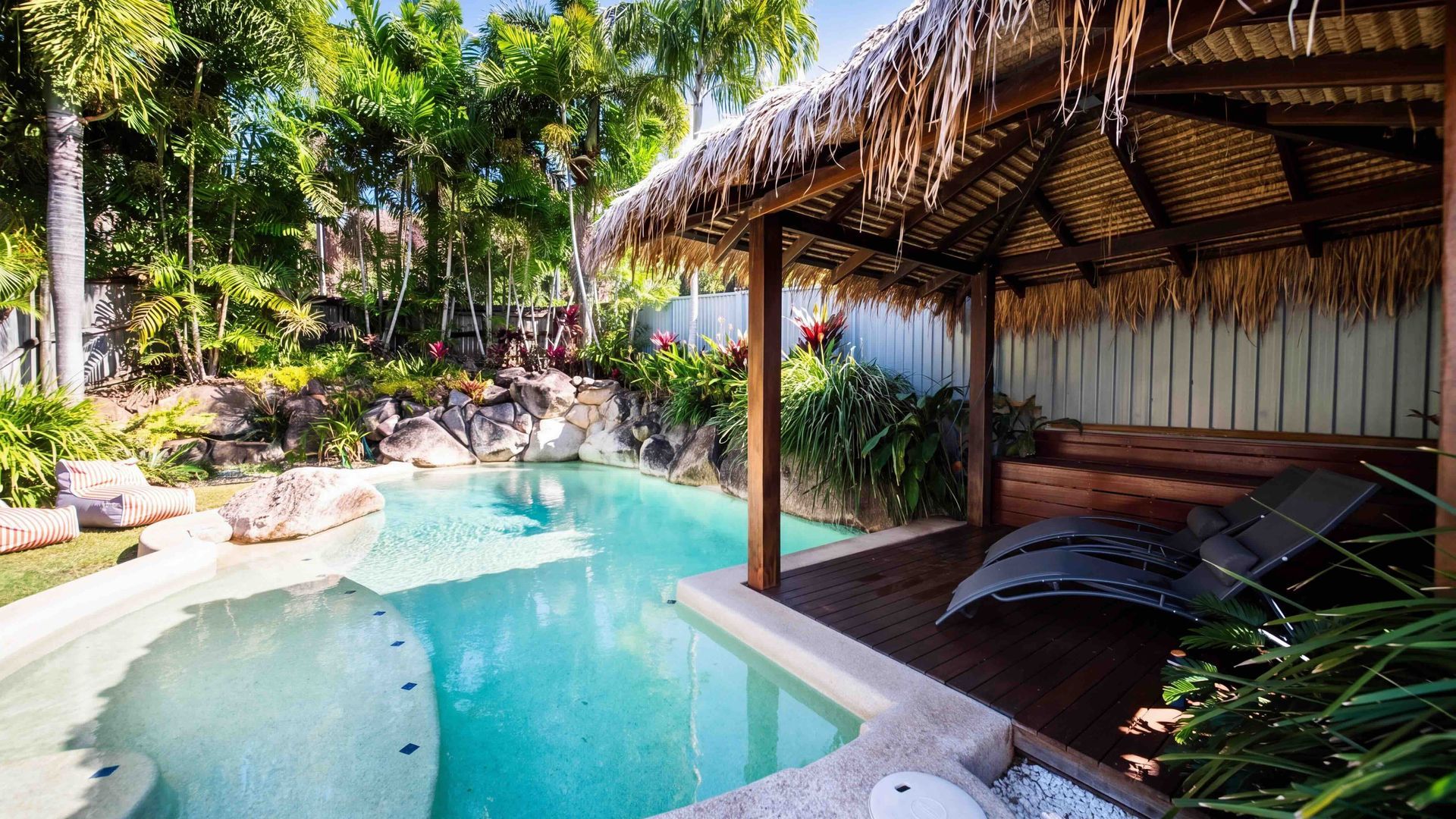 A pool area with a thatched-roof structure, lounge chairs, and tropical plants.