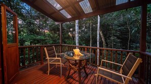 A wooden deck with a glass table and chairs, surrounded by a wooden railing, overlooking a forested area. - The Rainforest Nook Cairns (Kamerunga)