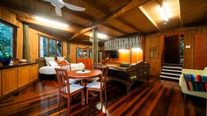 A wooden cabin interior with a bed, dining table, chairs, and a television. - The Rainforest Nook Cairns (Kamerunga)