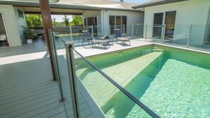 Une piscine séparée du reste par une paroi en verre, entourée d’une terrasse avec des chaises longues et un espace patio couvert.