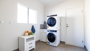 A laundry room with a washing machine, a dryer, a small white cabinet with drawers, a window, and a door. - The Retreat - South Mission Beach (South Mission Beach)