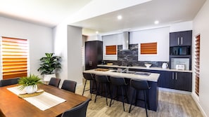 A modern kitchen with a central island, dark cabinetry, and a dining area with a wooden table and chairs. - The Retreat - South Mission Beach (South Mission Beach)