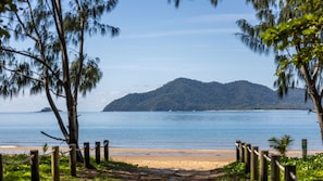 Une plage bordée d’une clôture en bois, un ciel dégagé et une montagne en arrière-plan.