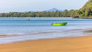 A beach with a green boat and a smaller boat in the distance, surrounded by a forested area and mountains. - The Retreat - South Mission Beach (South Mission Beach)