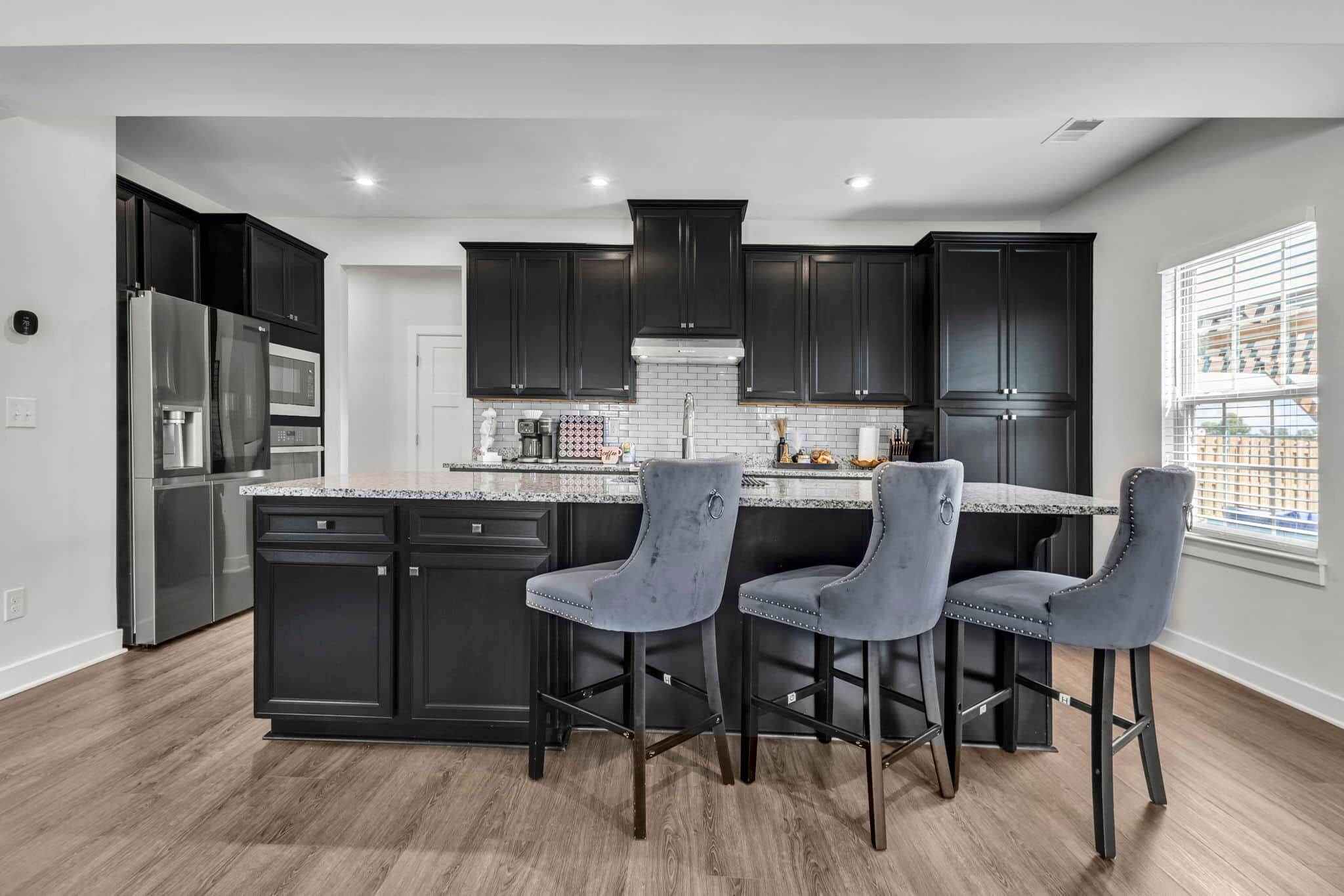 A modern kitchen with dark cabinetry, a stainless steel refrigerator, and a bar area with three bar stools.
