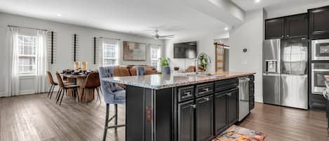 A modern kitchen with a central island, black cabinetry, stainless steel appliances, and a dining area with a wooden table and chairs.