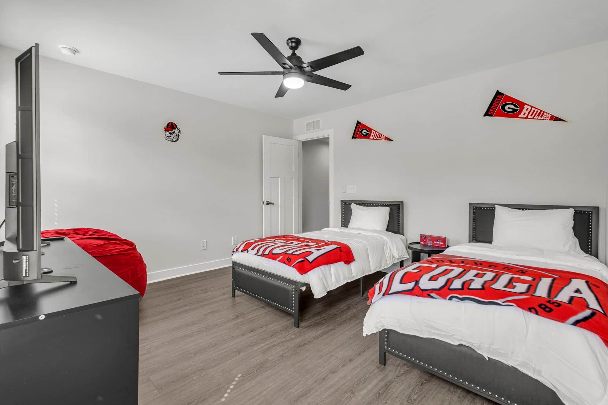 Quarto de hotel com duas camas, ventilador de teto, televisão e artigos de coleção do Georgia Bulldogs.