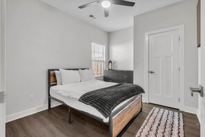 A bedroom with a bed, a nightstand, a window with blinds, a door, and a ceiling fan.