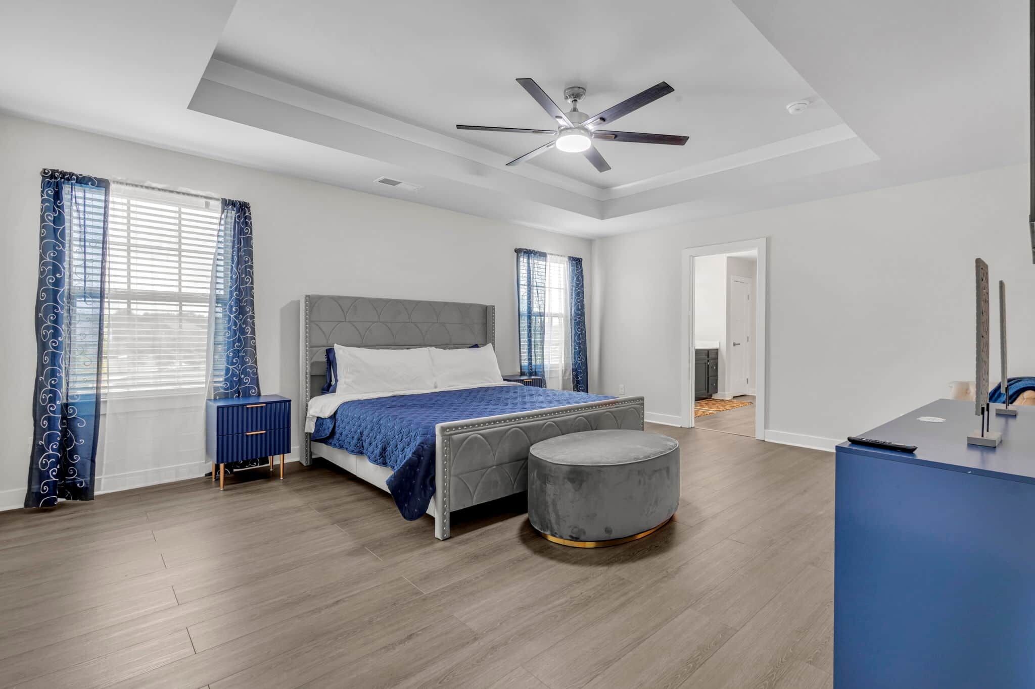 Un dormitorio moderno con una cama, un reposapiés redondo, un escritorio y un ventilador de techo.
