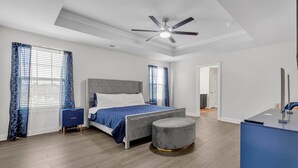 Ein modernes Schlafzimmer mit einem Bett, einem runden Hocker, einem Schreibtisch und einem Deckenventilator.