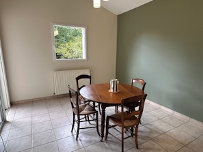 A dining area with a round wooden table, four chairs, a radiator, a window, and a view of greenery outside. - Country house with a pool between Bordeaux and St-Émilion (Croignon)