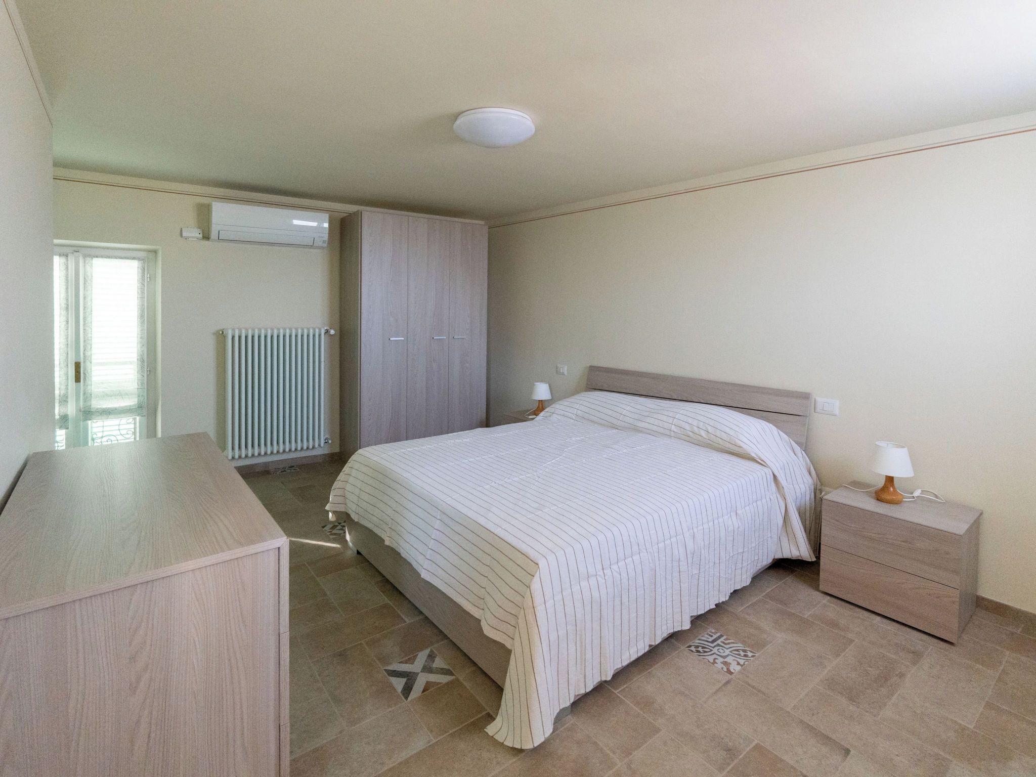 A bedroom with a bed, bedside tables, a wardrobe, and a radiator.