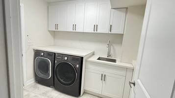 Un lavadero pequeño con dos lavadoras de carga frontal, un lavabo y armarios blancos.