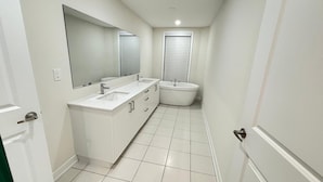 Un baño estrecho con lavamanos, espejo y bañera blancos.