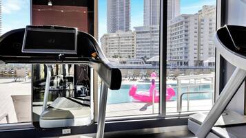 Academia com equipamentos de ginástica e vista para uma piscina com boia em formato de flamingo rosa.