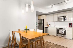 Uma cozinha moderna com eletrodomésticos de aço inoxidável, uma mesa de jantar de madeira e iluminação pendente.