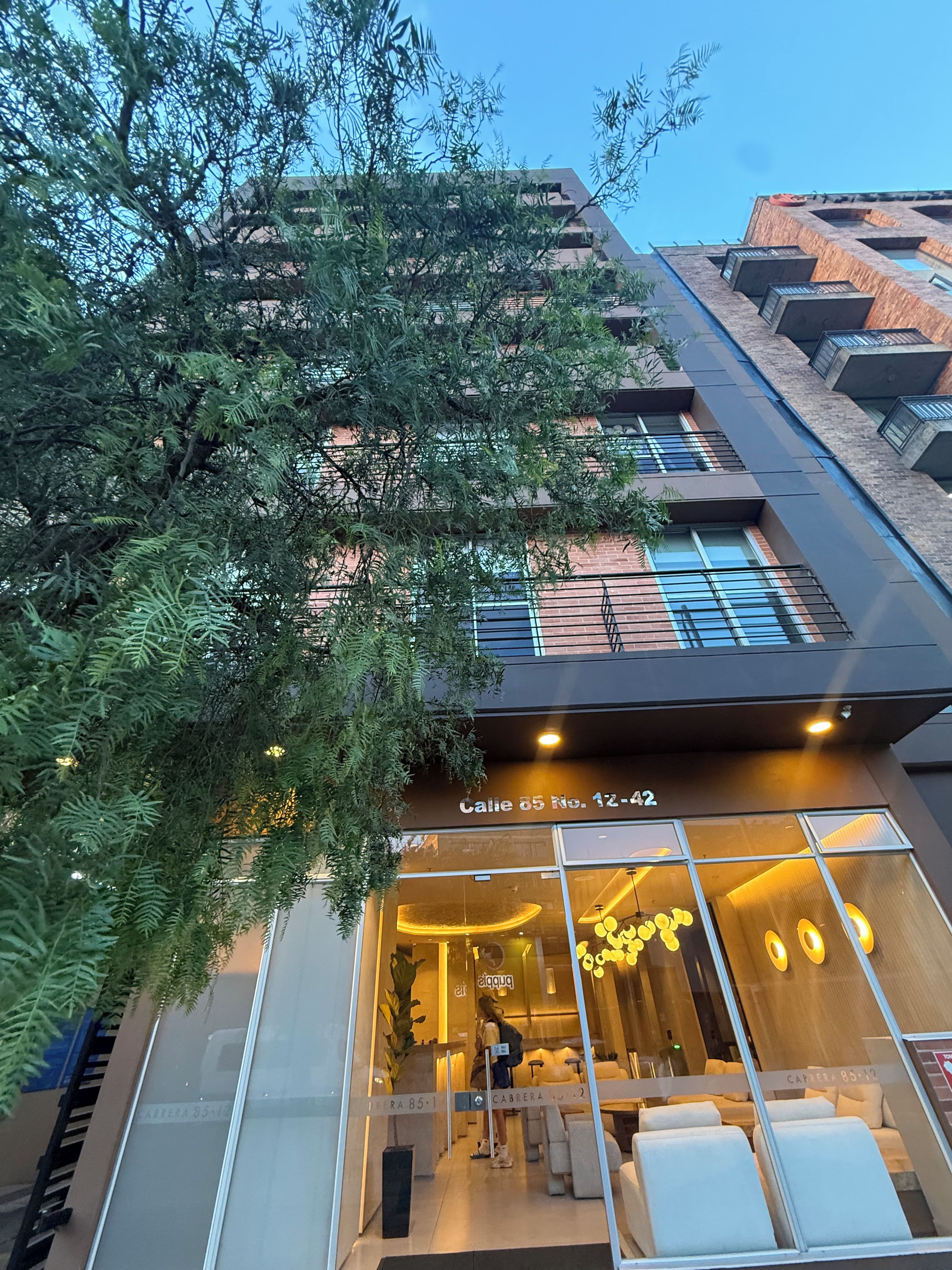 Un edificio moderno con fachada de vidrio, número visible y un letrero que indica un negocio o servicio en el interior.