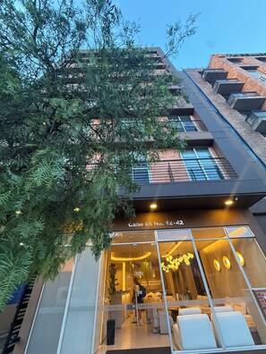 Un edificio moderno con fachada de vidrio, número visible y un letrero que indica un negocio o servicio en el interior.