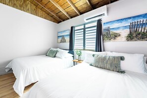 A hotel room with two beds, a wooden ceiling, a beach-themed painting, and a window with curtains. - Casa Macadamia Walk to Beach, Balneario & Boqueron (Cabo Rojo)