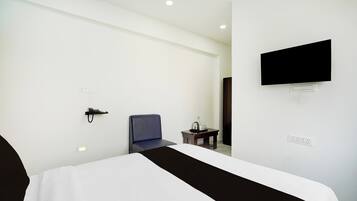 Habitación de hotel con cama, una silla, una mesita con una botella y vasos, teléfono, televisor montado en la pared y toma de corriente.