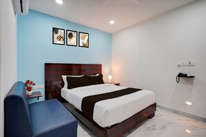 Une chambre d’hôtel moderne avec un grand lit, des tables de chevet, un bureau et un canapé bleu.