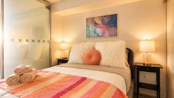 A hotel room with a bed, two bedside lamps, a painting on the wall, and a window with blinds.