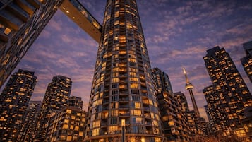 Un edificio de gran altura con varios pisos, rodeado de otros edificios altos, y una torre destacada al fondo.