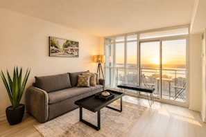 Un salon moderne avec un canapé, une table basse et une vue sur le paysage urbain, visible à travers de grandes fenêtres.