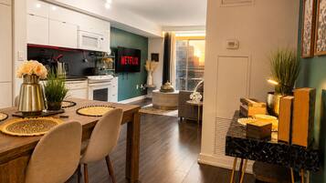 A modern kitchen with a flat-screen TV, a dining area with a wooden table and chairs, and a living space with a sofa and a coffee table.