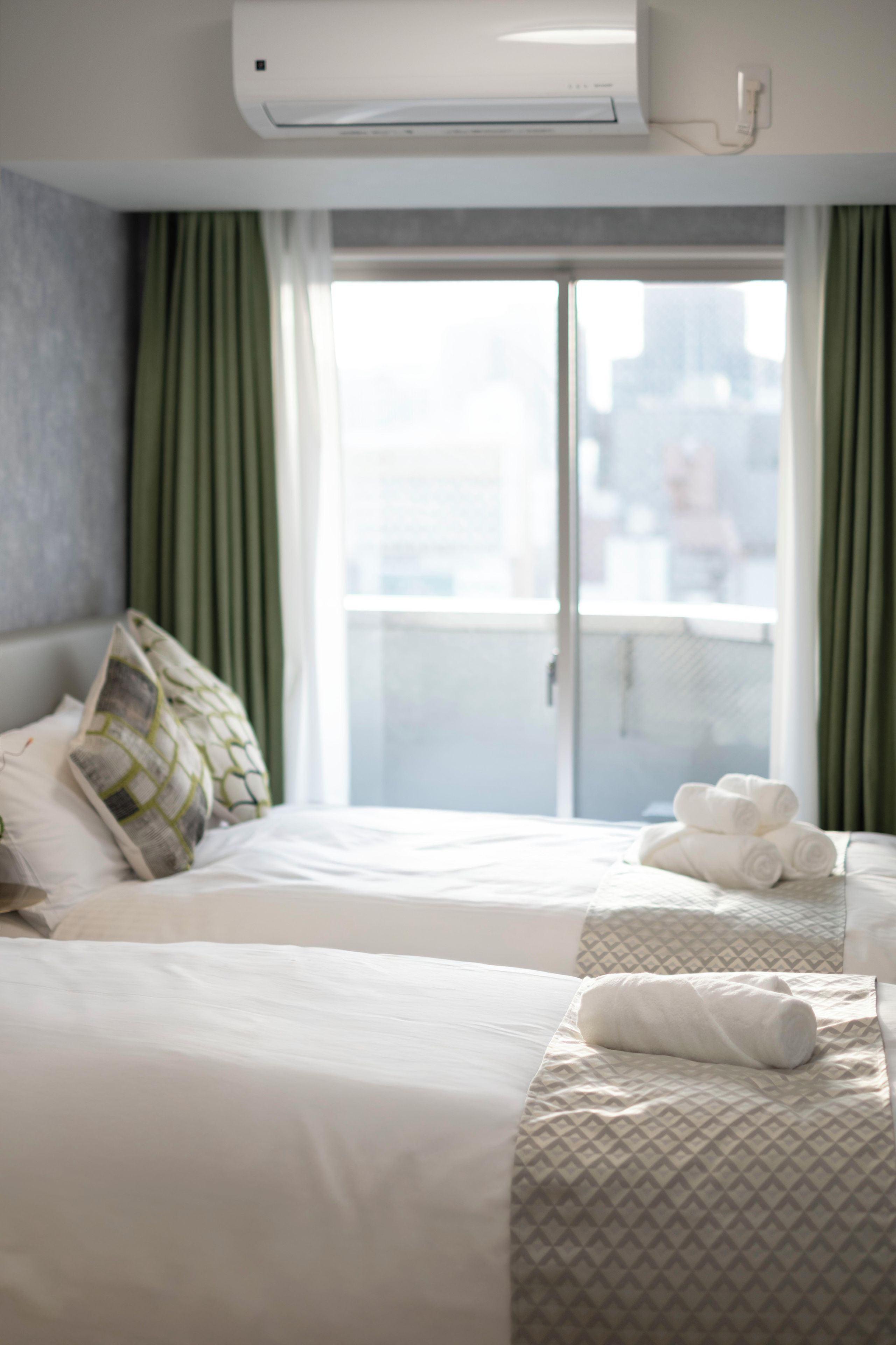 A hotel room with two beds, a large window with curtains, and a view of the city.