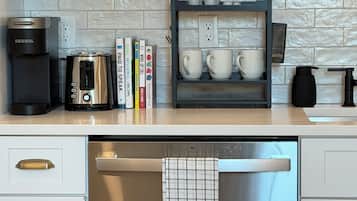 A kitchen with white cabinets, a coffee maker, a toaster, a dish rack with mugs, and a dishwasher.