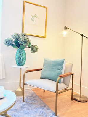 Une pièce comprenant une chaise, une petite table, un lampadaire et un tableau encadré accroché au mur.
