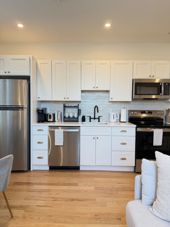 A modern kitchen with white cabinets, stainless steel appliances, and a wooden floor.