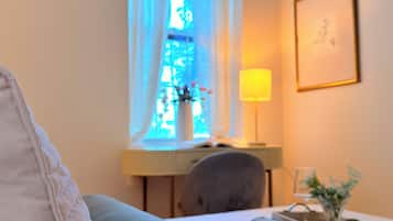 A hotel room with a bed, a desk with a lamp, a chair, and a window with a view of a building.