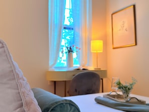 A hotel room with a bed, a desk with a lamp, a chair, and a window with a view of a building.
