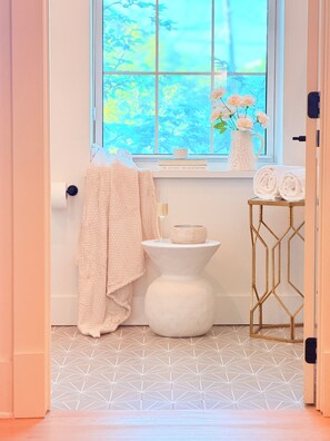 A bathroom with a toilet, a towel, a glass of water, and a window with a view of trees.
