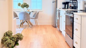 Una cocina moderna con armarios blancos, electrodomésticos de acero inoxidable y un comedor con mesa y sillas.
