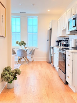 A modern kitchen with white cabinets, stainless steel appliances, and a dining area with a table and chairs. - East Side 1BR near Brown & RISD, Parking, Kitchen & W/D (Providence)
