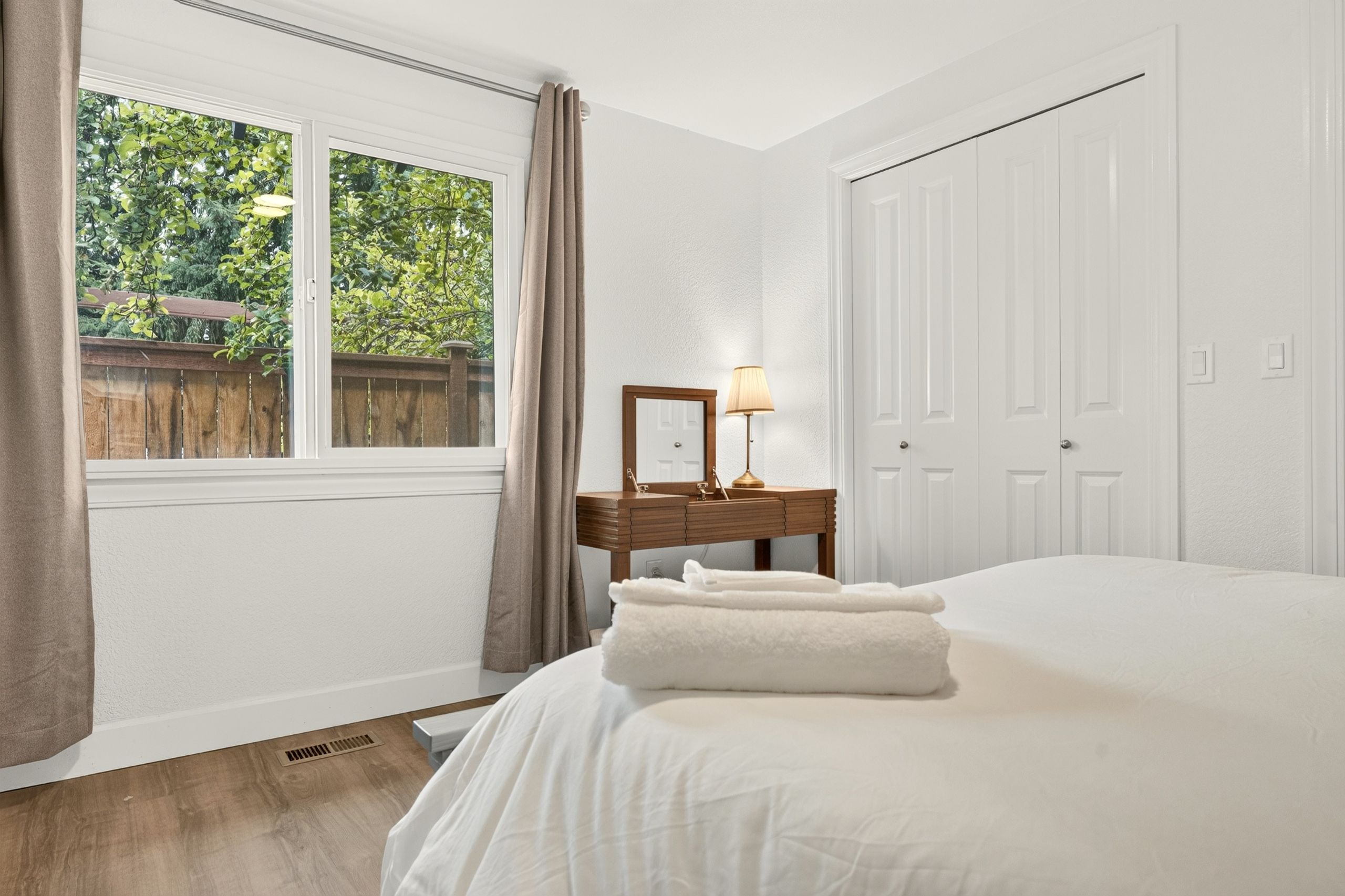 A bedroom with a bed, a nightstand with a lamp, a window with curtains, and a door.