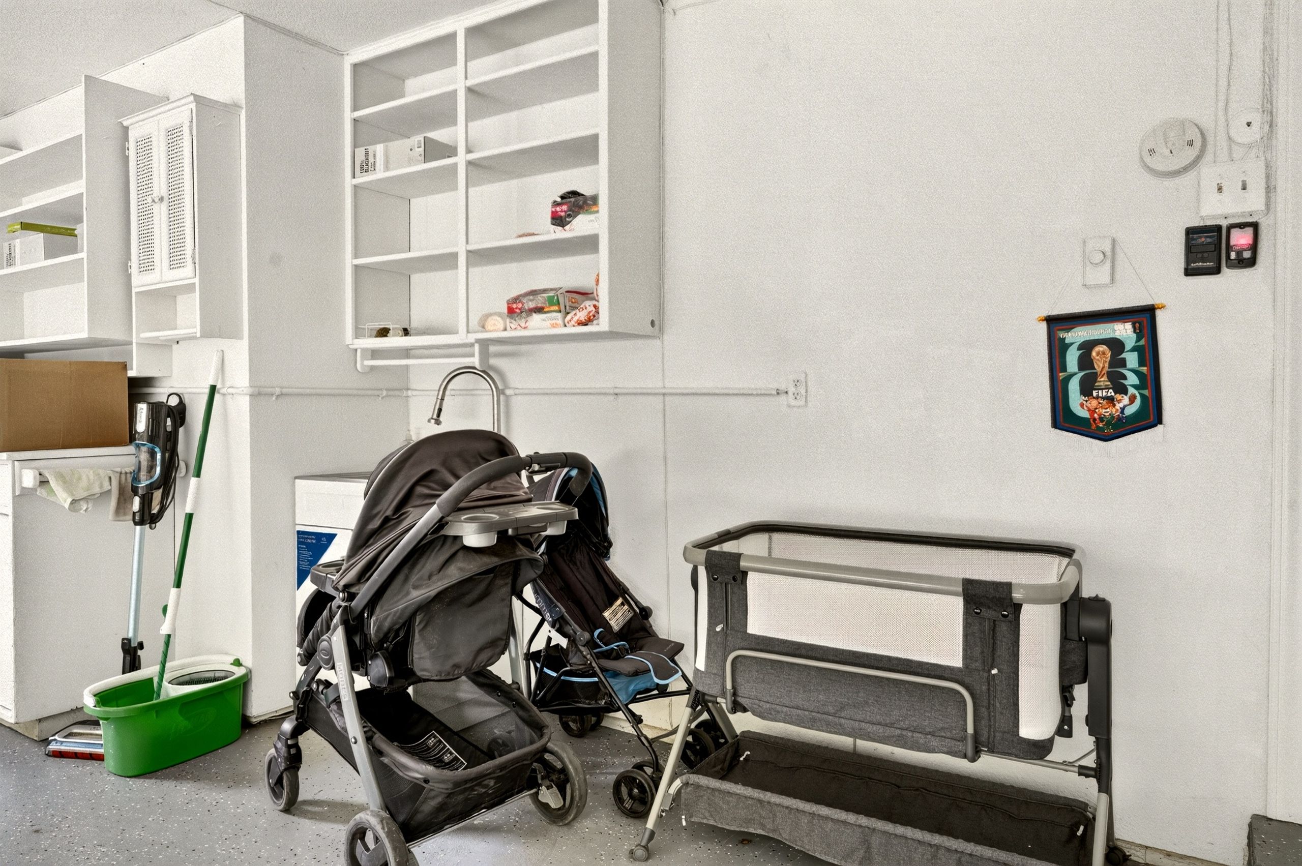 A room with a crib, a stroller, a shelf with items, and a picture on the wall.